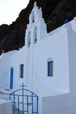 Yunan bayrağıyla beyaz bir Yunan Ortodoks Kilisesi manzarası ve arka planda ünlü kırmızı plajın volkanik manzarası