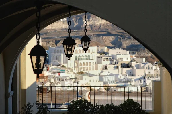 Bir kilisenin çatısında asılı fenerler ve arka planda Fira Santorini köyü.