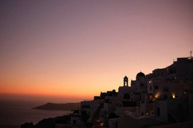 Fira Santorini 'de bir kiliseye çıkan aydınlık bir sokak ve renkli bir gün batımı.