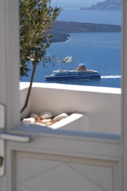 Santorini, Yunanistan - 10 Mayıs 2021: Zeytin ağacı, feribot ve Santorini volkanı manzaralı bir kapı