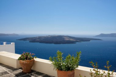 Nea Kameni volkanının panoramik manzarası Santorini 'deki saksılarla süslenmiş bir çatıdan.