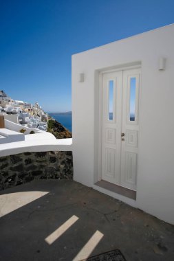 Tipik tasarım beyaz dekorasyon kapısı. Sokağın yanında Fira köyü ve Santorin 'deki Ege Denizi nefes kesici manzaralı.