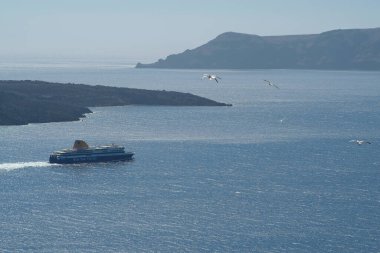 Santorini, Yunanistan - 10 Mayıs 2021 - Santorini 'deki Athinios limanından ayrılan bir feribot ve etrafta uçan martılar