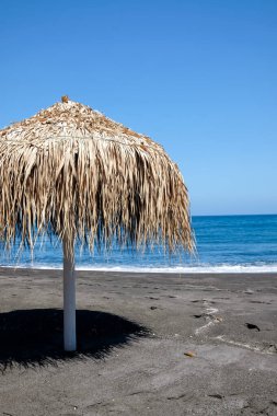 Perissa Santorini Yunanistan 'ın ünlü kumlu siyah plajında bir güneş şemsiyesi