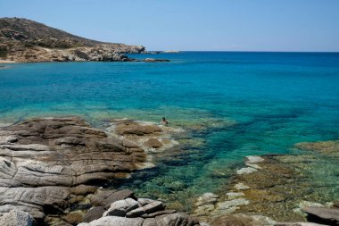 Ios, Yunanistan - 12 Haziran 2021: Yunanistan 'daki muhteşem kayalık Pikri Nero plajı yakınlarında banyo yapan bekar bir kadın