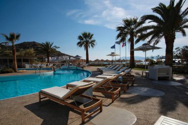 Ios, Yunanistan - 12 Haziran 2021: Yunanistan 'daki Mylopotas plajı önünde güneşli yataklı ve palmiye ağaçlı bir açık havuz manzarası