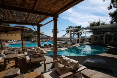 Ios, Yunanistan - 12 Haziran 2021: Yunanistan 'daki Mylopotas plajı önünde güneşli yataklı ve palmiye ağaçlı bir açık havuz manzarası