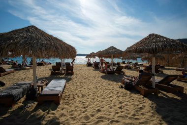 Ios, Yunanistan - 12 Haziran 2021: Güneşli yataklarda uzanan turistler ve Ios 'taki inanılmaz ve ünlü Mylopoatas plajının keyfini çıkarıyorlar