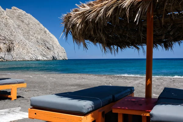 Boş güneş yatakları ve güneş şemsiyeleri Santorini 'nin ünlü kumlu plajı Perissa' da.