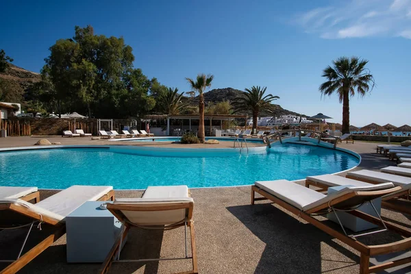 Ios, Yunanistan - 12 Haziran 2021: Yunanistan 'daki Mylopotas plajı önünde güneşli yataklı ve palmiye ağaçlı bir açık havuz manzarası