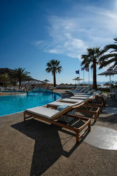 Ios, Yunanistan - 12 Haziran 2021: Yunanistan 'daki Mylopotas plajı önünde güneşli yataklı ve palmiye ağaçlı bir açık havuz manzarası