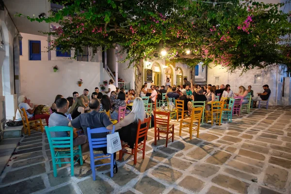 Ios, Yunanistan - 13 Haziran 2021: Turistler Ios köyündeki renkli bir açık hava barında içki içip canlı Yunan müziği dinliyorlar