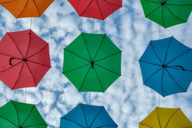 Renkli asılı şemsiyeler ve arkada bulutlu mavi bir gökyüzü.