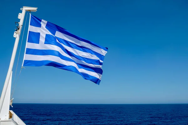 Huge greek flag of a ferry boat waving in the wind and the Aegean Sea in the background 