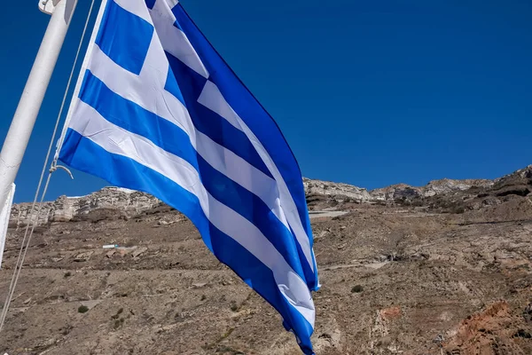 Huge greek flag waving in the wind in front of the island Santorini in Greece