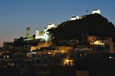 Panoramic view of the picturesque illuminated island of Ios in Greece with its famous palm tree and churches, while the sun is setting