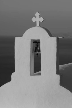 Yunanistan 'daki bir ortodoks kilisesinin tepesinde haç ve çan. Güneş arka planda siyah beyaz batarken.