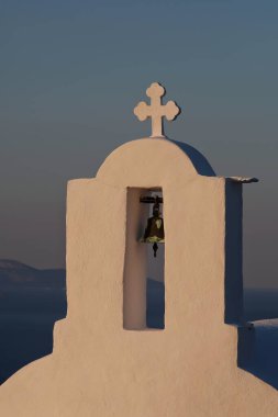 Güneş arka planda batarken, Yunanistan 'daki bir ortodoks kilisesinin tepesinde bir haç ve çan.