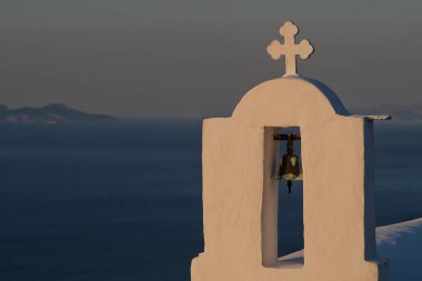 Güneş arka planda batarken, Yunanistan 'daki bir ortodoks kilisesinin tepesinde bir haç ve çan.