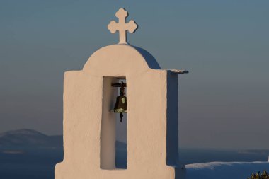 Güneş arka planda batarken, Yunanistan 'daki bir ortodoks kilisesinin tepesinde bir haç ve çan.
