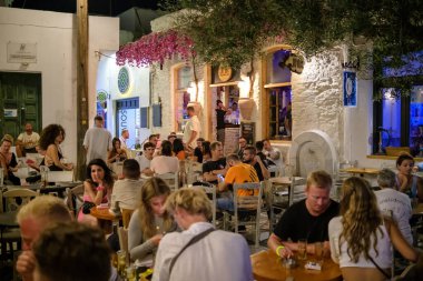 Ios, Yunanistan - 12 Eylül 2022: Barlarla çevrili genç turistler, gece vakti Yunanistan 'ın Ios kentindeki popüler meydanda içki ve kokteyl içiyorlar