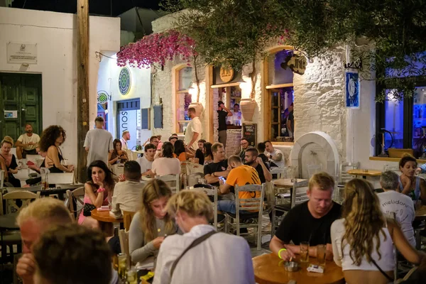 Ios, Yunanistan - 12 Eylül 2022: Barlarla çevrili genç turistler, gece vakti Yunanistan 'ın Ios kentindeki popüler meydanda içki ve kokteyl içiyorlar
