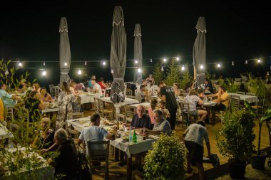 Nea Kallikrateia, Yunanistan - 28 Ağustos 2022: Yunanlılar ve turistler deniz kenarındaki samimi bir restoranda akşam yemeğinin keyfini çıkarıyorlar