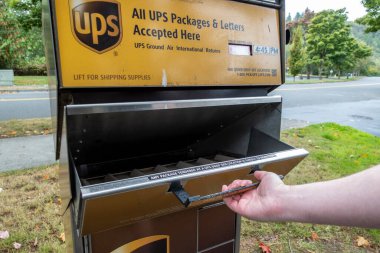 Kirkland, WA USA - Eylül 2021: Kirkland şehir merkezinde bir UPS paket ve posta mevduat istasyonu kapısını açan bir elin açısı