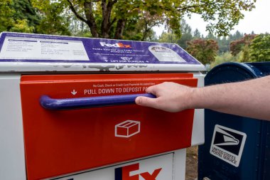 Kirkland, WA USA - Eylül 2021: Kirkland şehir merkezinde bir FedEx paketi ve posta mevduat istasyonu kapısını açan bir elin açısı