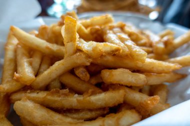 Ezilmiş ve kızartılmış, altın rengi patates kızartmalarının, restoran masasında beyaz kağıtlarla kaplı bir sepette yakın plan görüntüsü.
