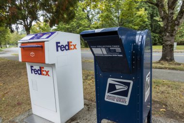 Kirkland, WA USA - Eylül 2021: Kirkland şehir merkezinde mavi bir USPS emanet kasasının yanındaki bir FedEx paketi ve posta mevduat istasyonunun açılı görünümü.