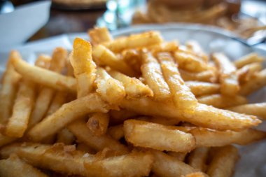 Ezilmiş ve kızartılmış, altın rengi patates kızartmalarının, restoran masasında beyaz kağıtlarla kaplı bir sepette yakın plan görüntüsü.
