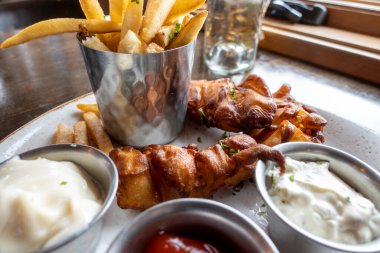 Bir restoranın içinde ketçaplı, tartar soslu ve çiftlik soslu kalın patates kızartmalı balık filetosu yakın çekim.
