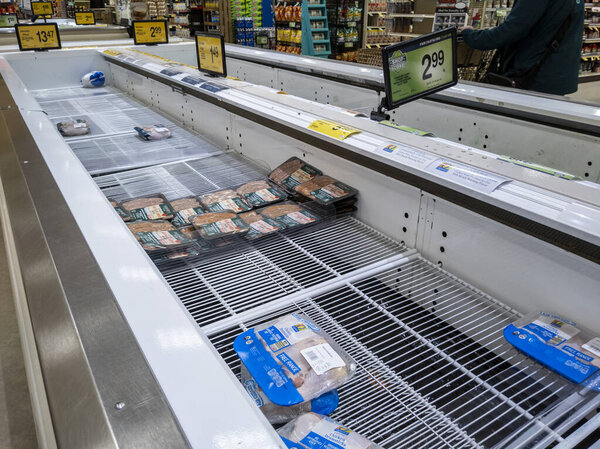 Kirkland, WA USA - circa January 2022: Angled view of food shortage in the refrigerated meats aisle in a Safeway grocery store during heavy snow storms across Washington.