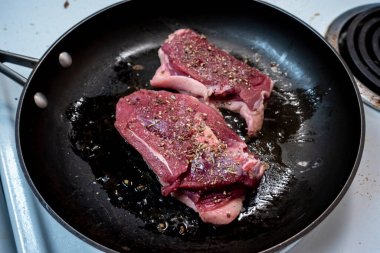 Beyaz bir sobanın tepesinde siyah tavada kızaran iki sulu ördek göğsüne odaklan.