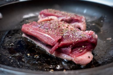 Beyaz bir sobanın tepesinde siyah tavada kızaran iki sulu ördek göğsüne odaklan.