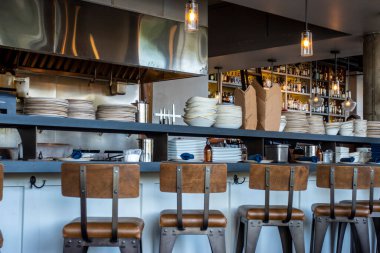Angled view of metal and wood bar stools at a bar countertop inside a restaurant, with no people around