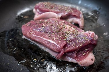 Beyaz bir sobanın tepesinde siyah tavada kızaran iki sulu ördek göğsüne odaklan.