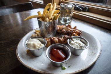 Bir restoranın içinde ketçaplı, tartar soslu ve çiftlik soslu kalın patates kızartmalı balık filetosu yakın çekim.