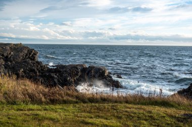 Beyaz, köpüklü dalgalar San Juan Adası, WA 'da gün batımında kıyı kayalarına çarpıyor.