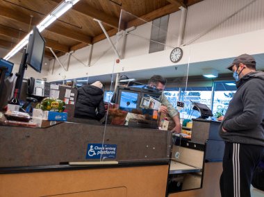 Kirkland, WA USA - Aralık 2021: Coronavirus salgını sırasında bir PCC marketinde pleksiglas bölme arkasında bir erkek kasiyerin görüntüsü.