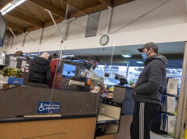 Kirkland, WA USA - Aralık 2021: Coronavirus salgını sırasında bir PCC marketinde pleksiglas bölme arkasında bir erkek kasiyerin görüntüsü