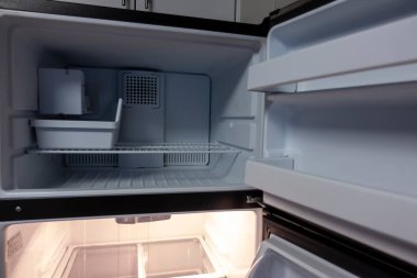 Beyaz, boş bir buzdolabı manzarası. Kapısı sonuna kadar açık. Birkaç raf ve yiyeceksiz çekmece görmek için.