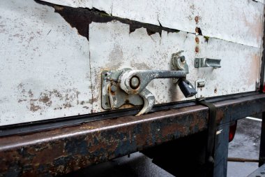 Beyaz hareket eden bir kamyonun arkasındaki paslı metal bir mandalın siyah basamaklı merdiveni yakın plan görüntüsü.