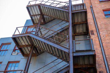 Kırmızı tuğlalı bir binanın dışındaki ahşap merdivenin alçak açılı görüntüsü bir apartmanın ya da iş yerinin farklı seviyelerine çıkıyor.