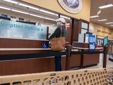 Kirkland, WA USA - Ekim 2021: Beyzbol şapkalı bir kadının Safeway 'deki bir marketten reçete alırken görüntüsü