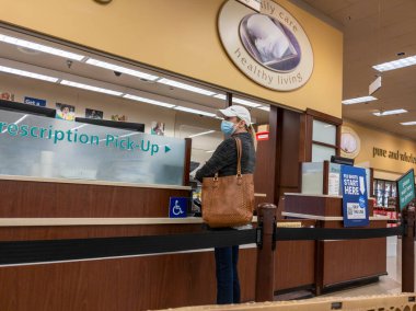 Kirkland, WA USA - Ekim 2021: Beyzbol şapkalı bir kadının Safeway 'deki bir marketten reçete alırken görüntüsü