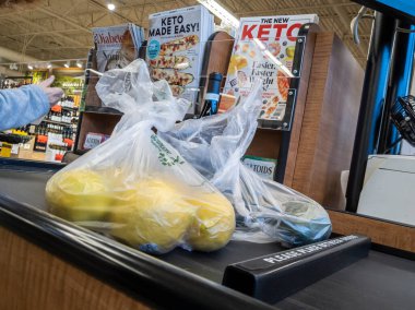 Mill Creek, WA USA - circa April 2022: Angled view of a customer placing bagged produce on a conveyor belt to be purchased inside a Town and Country grocery store.