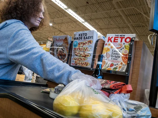 Mill Creek, WA USA - Nisan 2022: Bir kasaba ve ülke marketinden satın alınmak üzere poşetlenmiş ürünleri bir taşıma bandına yerleştiren bir müşterinin açılı görünümü