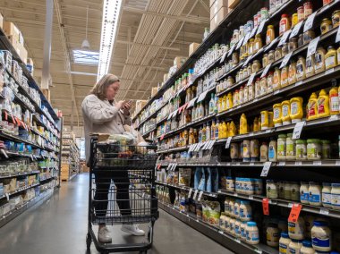 Mill Creek, WA USA - Nisan 2022: Bir kasaba ve taşra marketinin içindeki baharat ve salata sosu reyonunda alışveriş yapan bir kadının düşük açılı görüntüsü.